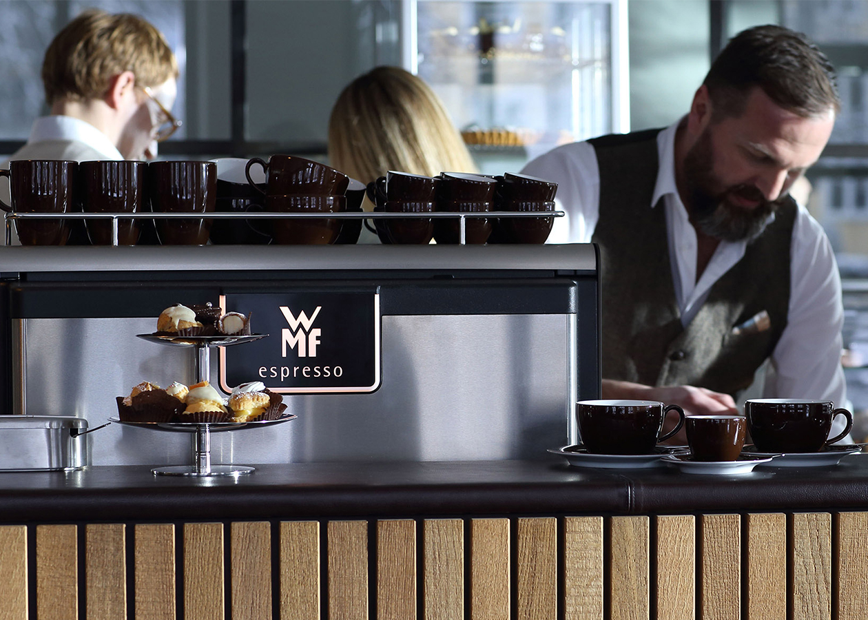 Ein Barista serviert kunstvoll Kaffee, zubereitet mit der WMF espresso, einem Kaffee-Halbautomat für die Gastronomie und Catering. Entworfen wurde das schlüssige Design von dem Designstudio designship GmbH aus Ulm. WMF espresso - Siebträger - Kaffee-Halbautomat - iF Design Award 2015 - red dot award 2015 - best of the best - designship GmbH - Produktdesign - Industriedesign - Maschinendesign - Interfacedesign - iF world design index - Top 25 Industry - Top 100 design studios worldwide - we love design