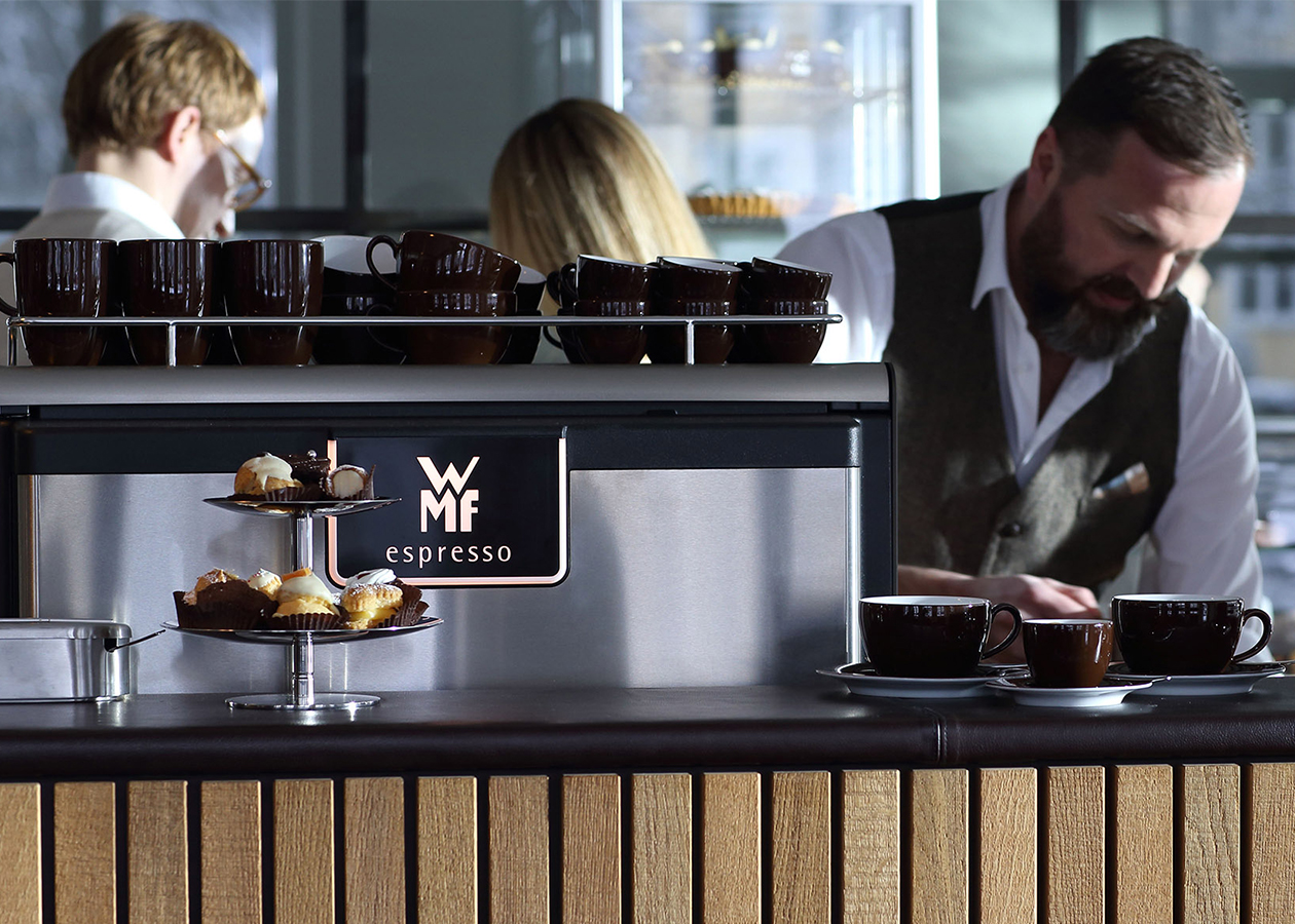 A barista artistically serves coffee, prepared with the WMF espresso, a semi-automatic coffee machine for gastronomy and catering. The coherent design was created by the design studio designship GmbH from Ulm. WMF espresso - portafilter - semi-automatic coffee machine - iF Design Award 2015 - red dot award 2015 - best of the best - designship GmbH - product design - industrial design - machine design - interface design - iF world design index - Top 25 Industry - Top 100 design studios worldwide - we love design